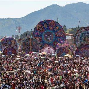 Auf einem Outdoor-Festival versammelt sich eine riesige Menschenmenge, um massive, aufwendig verzierte Drachen vor einer Bergkulisse zu bewundern.