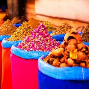 Gros plan sur des monticules coniques d'épices et de fleurs séchées présentés dans des sacs colorés sur un étal de marché.