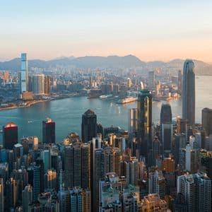 Una vista aerea di un fitto paesaggio urbano con molti grattacieli che circondano uno specchio d'acqua al tramonto, con le montagne sullo sfondo.