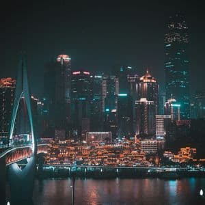 Un ponte illuminato attraversa un fiume con lo skyline luminoso di grattacieli di una città sullo sfondo di notte.