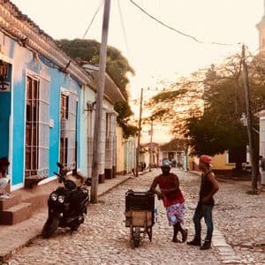Due uomini parlano su una strada acciottolata fiancheggiata da case coloniali colorate al tramonto.