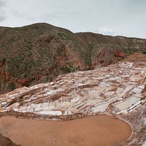 Salinas en terrazas, blancas y marrones, en la ladera de una montaña bajo un cielo cubierto.