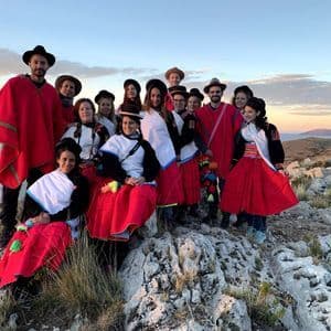 Un viaje en grupo de WeRoad con ropa tradicional roja y blanca posa en una colina rocosa con vistas a un cuerpo de agua al atardecer.
