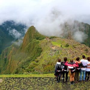 Un grupo de viaje de WeRoad, abrazados, contempla ruinas antiguas en una ladera verde y brumosa desde un mirador.