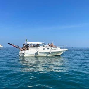 Un viaggio di gruppo WeRoad in relax su un motoscafo bianco in mare, con una scogliera sullo sfondo sotto un cielo azzurro.