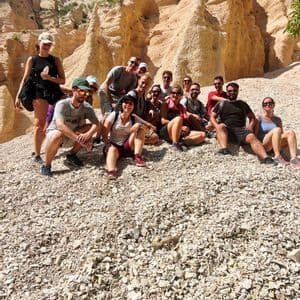 Un viaggio di gruppo WeRoad in posa per una foto su un pendio ghiaioso, con grandi formazioni rocciose erose sullo sfondo sotto un cielo blu.