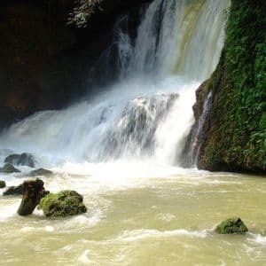 Una grande cascata precipita da una scogliera rocciosa e ricoperta di vegetazione in un fiume torbido sottostante.