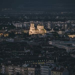 Una catedral iluminada con cúpulas doradas se erige en el centro de un extenso paisaje urbano nocturno.