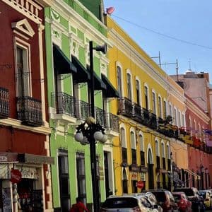 Una fila de coloridos edificios rojos, verdes y amarillos con balcones bordea una calle estrecha con coches estacionados.
