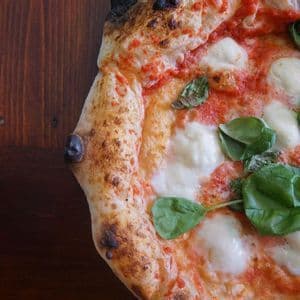 Un primo piano di una pizza Margherita napoletana con basilico fresco e mozzarella su un tavolo di legno scuro.