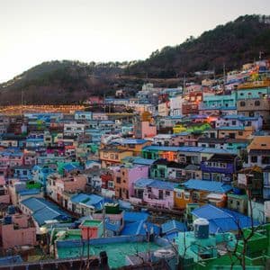 An overview of colorful, tightly packed houses built into a green hillside at sunset, with string lights illuminated.
