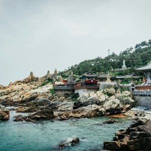 A traditional temple complex built on a rocky coastline, with a stone bridge connecting buildings over the turquoise sea.