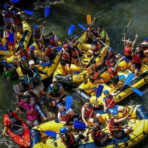 Vista aerea di un gruppo WeRoad in viaggio che posa su diverse zattere gialle su un fiume, con le pagaie alzate in aria.