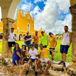 Eine WeRoad-Gruppe posiert für ein Foto unter einem Steinbogen, im Hintergrund ein großes gelbes Gebäude und ein Hund in der Nähe.