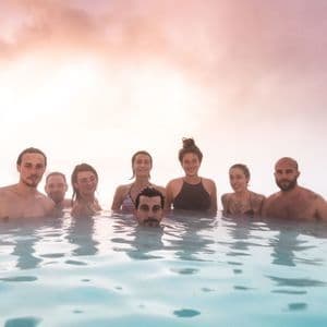 Eine WeRoad-Gruppenreise von lächelnden und entspannten Menschen im dampfenden, milchig-blauen Wasser eines Thermalbades.