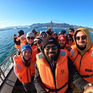 Un groupe WeRoad en gilets de sauvetage orange prend un selfie sur un bateau, naviguant entre icebergs et montagnes.