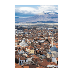 Veduta aerea di una città con tetti di tegole rosse, con montagne innevate che si ergono sullo sfondo sotto un cielo parzialmente nuvoloso.
