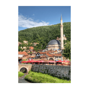 Una moschea con cupola e minareto domina una cittadina con edifici dai tetti rossi. In primo piano, un ponte di pietra attraversa un fiume.