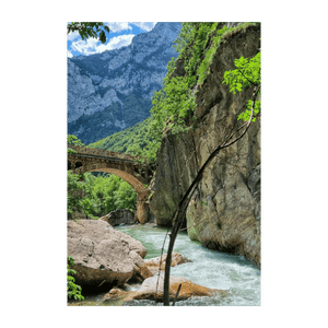 Un ponte ad arco in pietra attraversa un fiume turchese impetuoso in una gola di montagna lussureggiante e verde.