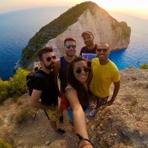 Un gruppo WeRoad si fa un selfie su una scogliera a picco su una costa rocciosa e il mare blu al tramonto.
