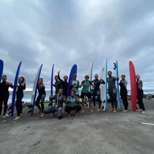 Un viaggio di gruppo WeRoad con persone in mute che posano con le loro tavole da surf su una passeggiata in riva all'oceano sotto un cielo nuvoloso.