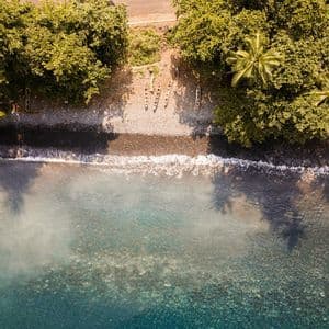 Una vista aerea dall'alto di canoe su una spiaggia di ciottoli, dove l'acqua cristallina turchese incontra una costa lussureggiante e alberata.