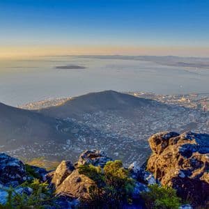 Une ville côtière et un pic montagneux vus d'un point de vue rocheux élevé sous un ciel clair au lever du soleil.