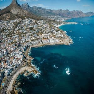 Une vue aérienne d'une ville sur un littoral rocheux, avec une chaîne de montagnes en arrière-plan sous un ciel bleu.