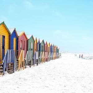 Une rangée de cabanes de plage en bois colorées se dressant sur une plage de sable blanc sous un ciel bleu clair.