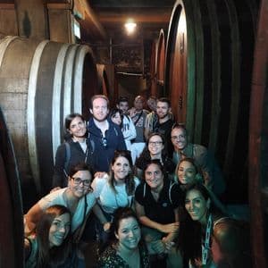 Un gruppo WeRoad in viaggio posa per una foto in una cantina tra grandi botti di legno.