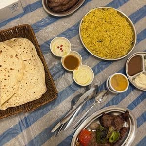 Un pasto tradizionale a base di riso giallo, carne alla griglia, pane azzimo e salse è servito su una tovaglia a righe.