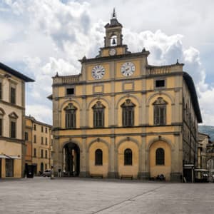 Un sontuoso edificio giallo con una torre dell'orologio si erge in una grande piazza lastricata sotto un cielo parzialmente nuvoloso.