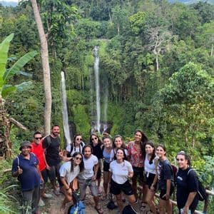 Eine WeRoad-Gruppe posiert auf einem Dschungelpfad für ein Foto, im üppigen Hintergrund ist ein hoher, mehrstufiger Wasserfall zu sehen.