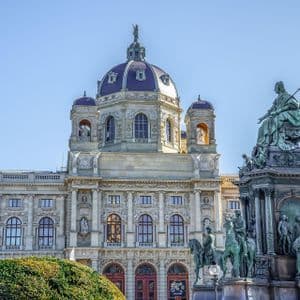 Un grand musée historique avec un dôme sombre et un monument en bronze orné au premier plan, vu par une journée claire et ensoleillée.