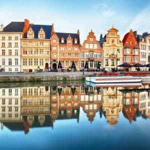 Des bâtiments colorés et historiques, aux toits à pignon, bordent un canal, leurs façades se reflétant dans l'eau calme en contrebas.