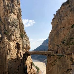 Un viaggio di gruppo WeRoad attraversa un ponte stretto sospeso tra due pareti rocciose a strapiombo di un canyon, con un fiume molto più in basso.