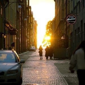 Menschen zeichnen sich vor einem goldenen Sonnenuntergang am Ende einer engen, kopfsteingepflasterten Stadtgasse ab.