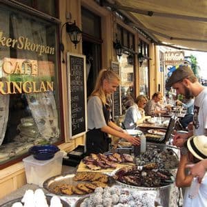Ein Verkäufer arbeitet an einem Stand eines Straßencafés und bietet Kunden eine Auswahl an frischem Gebäck, Keksen und Süßigkeiten an.
