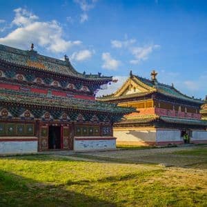 Un complejo de templos asiáticos tradicionales con techos de tejas verdes ornamentadas en un campo de hierba bajo un cielo azul.