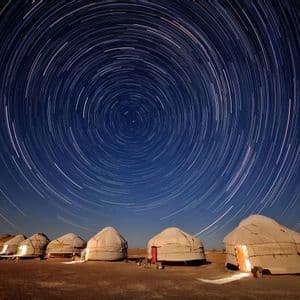 Una fila de yurtas iluminadas se asienta en el suelo por la noche bajo un cielo con rastros circulares de estrellas de larga exposición.