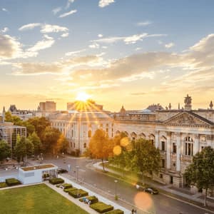 Luftaufnahme einer Stadtlandschaft mit historischem Gebäude und großer Kuppel, gebadet im goldenen Licht der untergehenden Sonne.