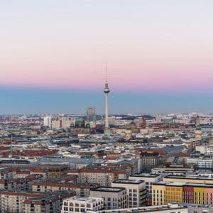 Luftaufnahme der Berliner Skyline mit dem Fernsehturm im Mittelpunkt unter einem rosa-blauen Verlaufs-Himmel bei Sonnenuntergang.
