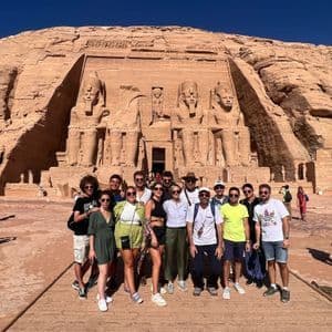 Un groupe WeRoad en voyage, posant pour une photo devant un grand temple taillé dans la roche, orné de quatre statues colossales assises.