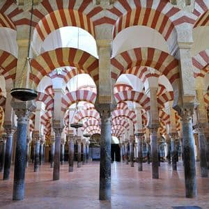 Un gran salón con hileras repetitivas de columnas de piedra que sostienen arcos de doble altura a rayas rojas y blancas.