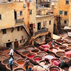 Hommes travaillant dans une tannerie traditionnelle en plein air, entourés de grandes cuves circulaires en pierre remplies de teintures colorées.
