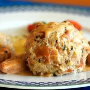 Nahaufnahme von zwei großen Semmelknödeln und Fleischstücken, bedeckt mit einer cremigen Soße auf einem dekorativen Teller.