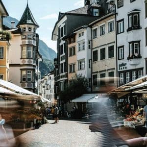 Langzeitaufnahme eines Kopfsteinpflaster-Straßenmarktes, mit unscharf vorbeiziehenden Menschen zwischen Ständen und historischen Gebäuden.