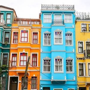 Una hilera de edificios estrechos y de varias plantas pintados en tonos vibrantes de verde azulado, naranja, azul y amarillo.