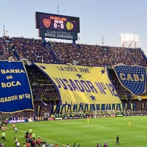 Uno stadio del Boca Juniors gremito con tifosi che espongono grandi striscioni blu e gialli prima di una partita di calcio.