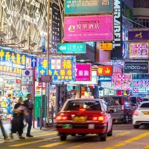 A busy city street at night with motion-blurred cars and pedestrians under dense, glowing neon signs with Chinese characters.